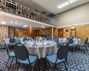A conference room with round tables, blue chairs, a staircase, and a brick wall.