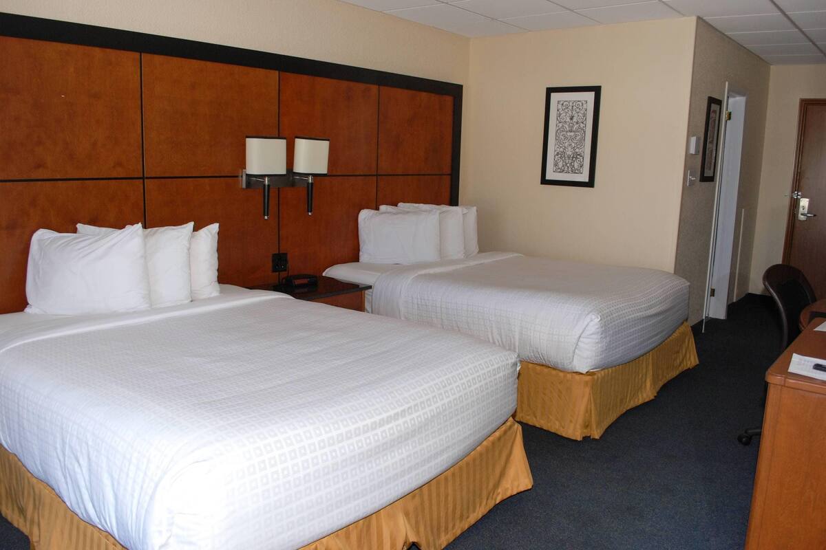 A hotel room with two beds, a wooden headboard, a nightstand, a desk, and a framed picture on the wall.