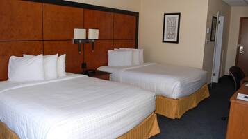 A hotel room with two beds, a wooden headboard, a nightstand, a desk, and a framed picture on the wall.