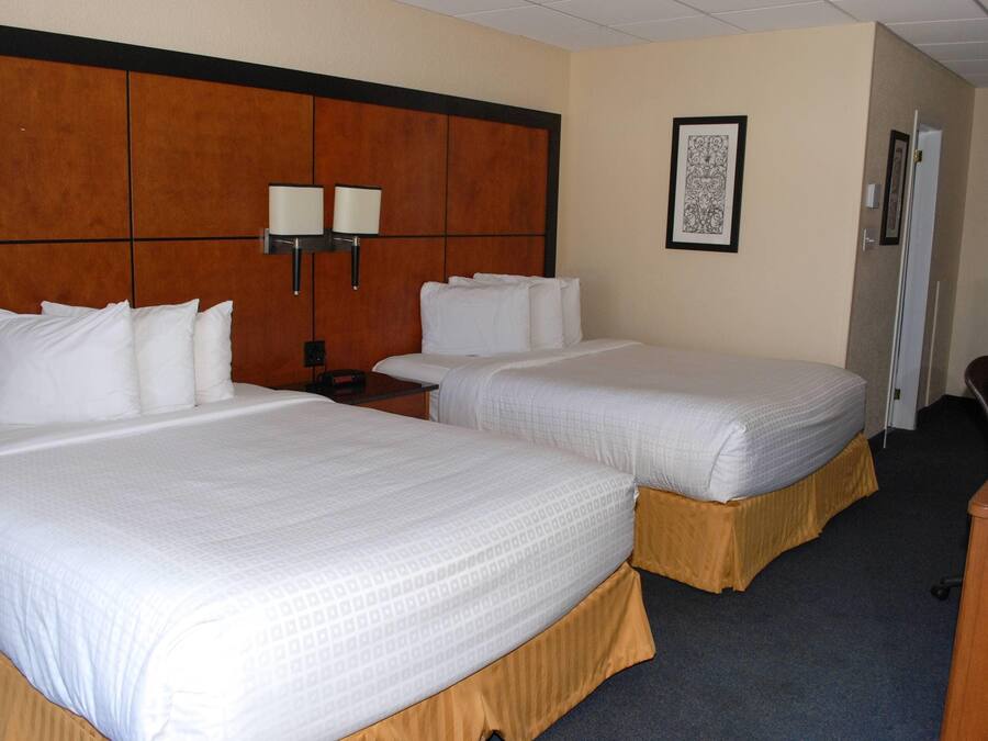 A hotel room with two beds, a wooden headboard, a nightstand, a desk, and a framed picture on the wall.
