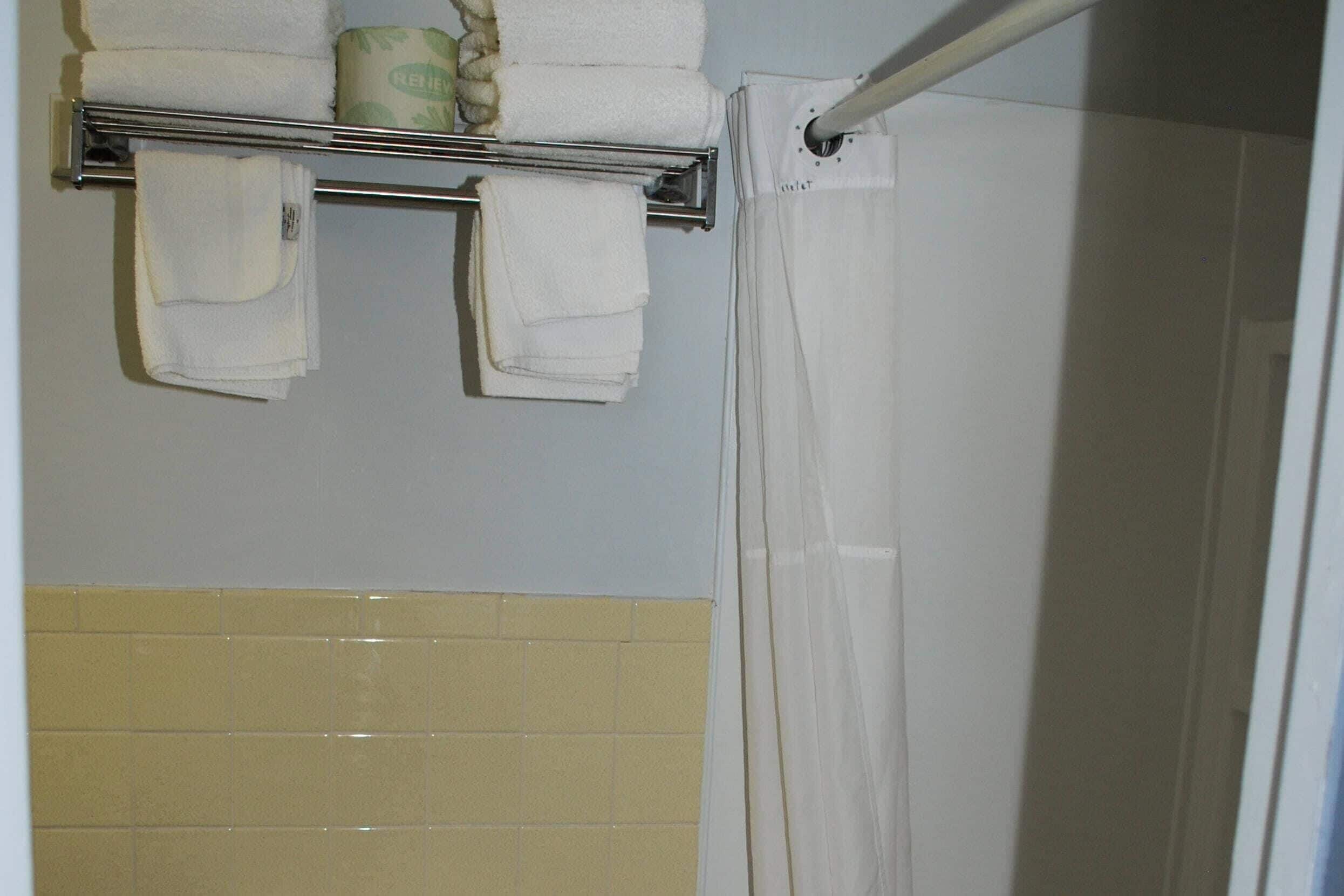 A bathroom with a towel rack holding folded towels, a shower curtain, and a yellow-tiled wall.