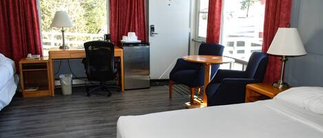A hotel room with a bed, desk, chair, and a refrigerator.