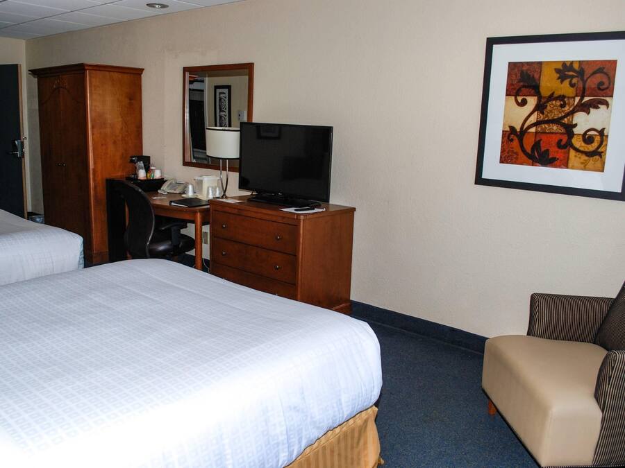 Habitación de hotel con dos camas, un escritorio con computadora, una silla, un televisor y un cuadro en la pared.