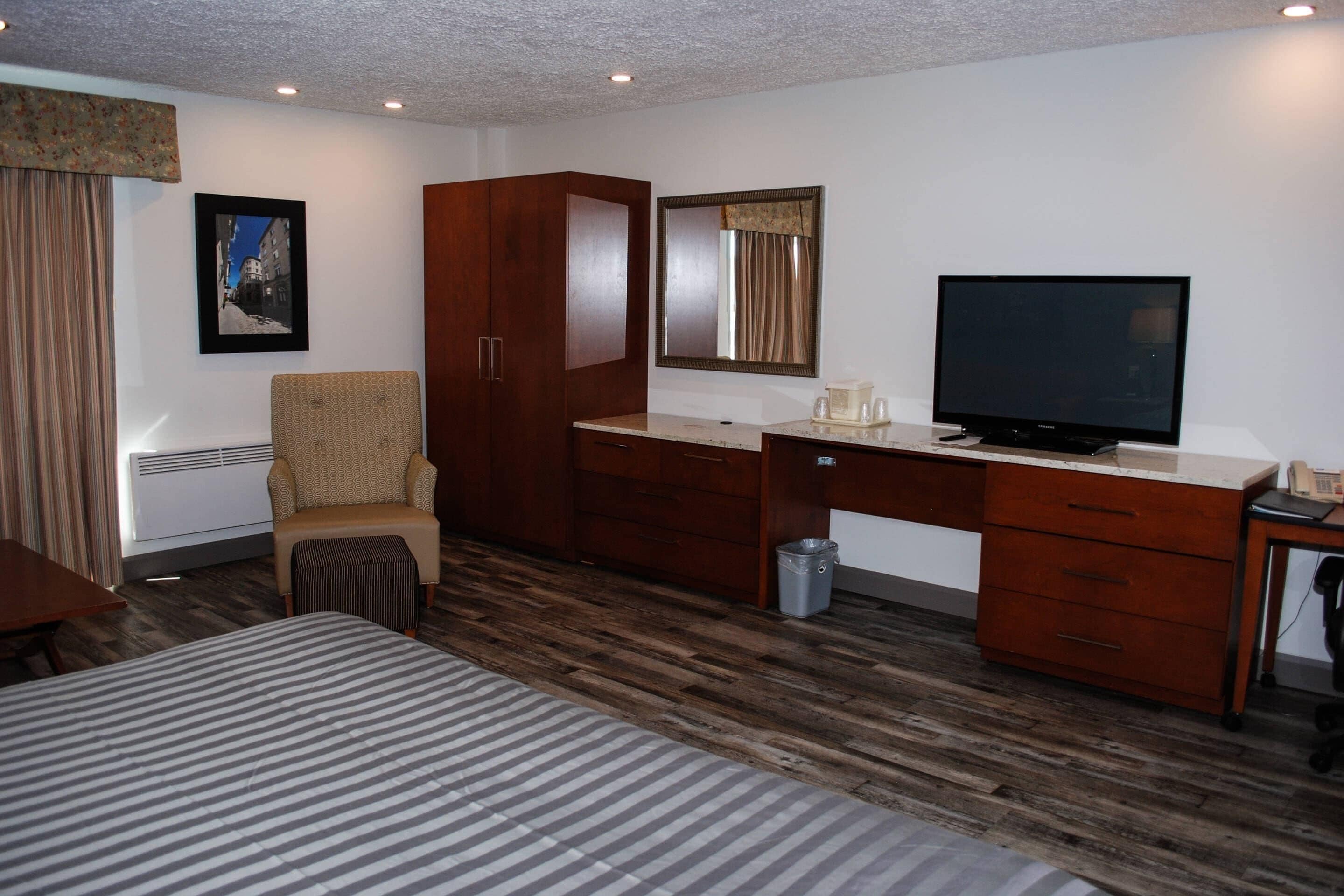 A hotel room with a bed, a desk with a television, a chair, a wardrobe, and a waste bin.
