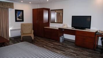 A hotel room with a bed, a desk with a television, a chair, a wardrobe, and a waste bin.