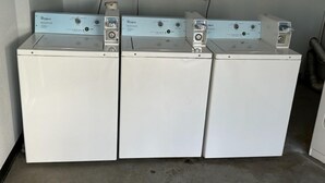 Tre frontbetjente Whirlpool vaskemaskiner på række, hver med kontrolpanel og strømkabel tilsluttet.