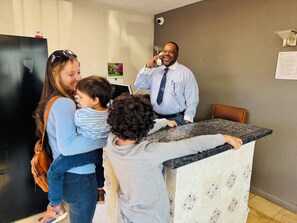 A family interacting with a receptionist in a hotel lobby with a modern design, a reception desk, and a wall-mounted security camera. - Newnan Nook (Newnan)