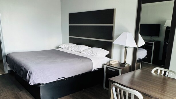 Et hotelværelse med seng, natbord, lampe og et spisebord med stole.