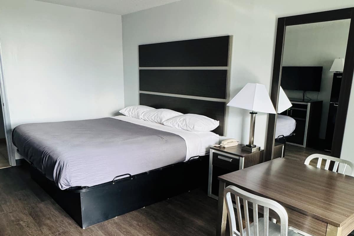 A hotel room with a bed, bedside table, lamp, and a dining table with chairs.