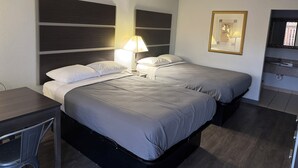 Et hotelværelse med to senge, et skrivebord, en stol, et fjernsyn og et billede i ramme på væggen.