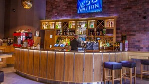 A bar with a wooden counter, shelves with bottles, and a TV screen displaying '50 MILLION'. - Columba Hotel (Oban)