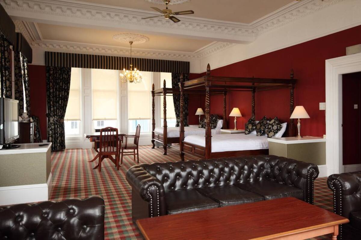 A room with a four-poster bed, a leather sofa, a wooden table, and a chandelier.