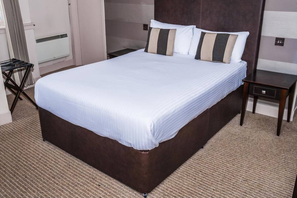 A neatly made bed with a dark headboard and white bedding in a hotel room.