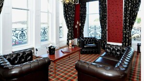 A room with a checkered floor, black leather sofas, a wooden coffee table, and a chandelier. - Columba Hotel (Oban)