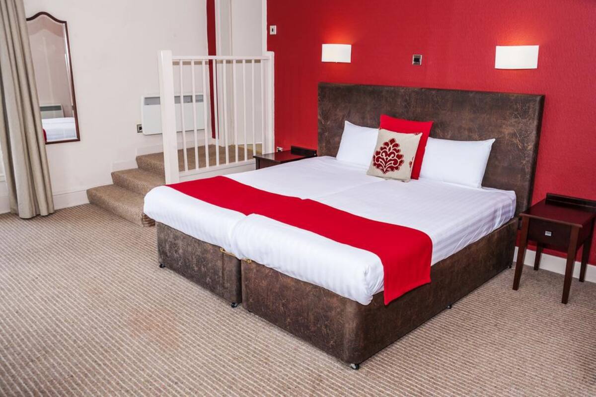 A hotel room with a large bed, red walls, and a staircase.