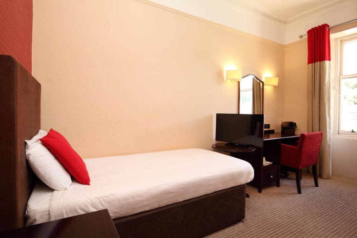 A hotel room with a bed, a desk, a chair, a TV, and a mirror.