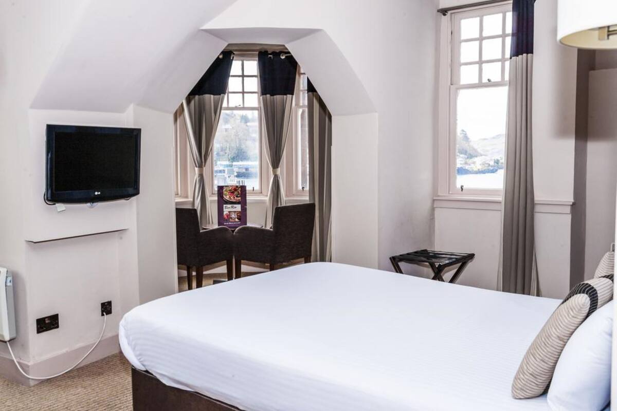 A hotel room with a bed, a TV mounted on the wall, a small table, and a chair.