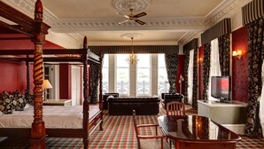 A hotel room with a checkered floor, a four-poster bed, a sofa, a dining table, and a television. - Columba Hotel (Oban)