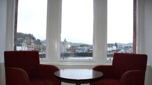 A room with two red chairs and a small table, large windows with a view of a cityscape. - Columba Hotel (Oban)