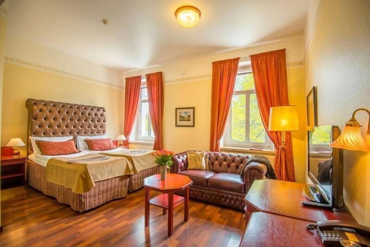 A hotel room with two beds, a sofa, a small table, and a desk with a lamp.