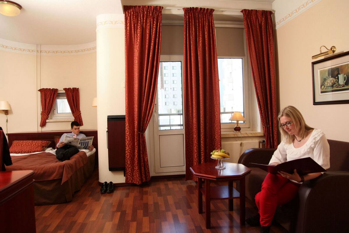 A hotel room with two beds, a dining table with fruit, and a person reading a book.
