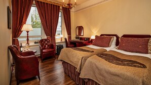 A hotel room with two beds, a desk, a chair, and a large window with curtains. - Hotel Astor (Vaasa)