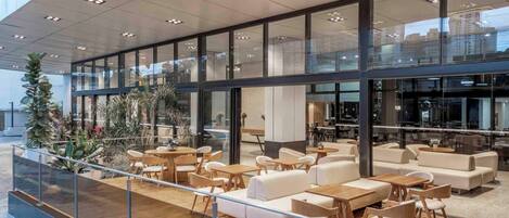 Un espacio interior moderno con terraza de madera, zonas de estar y fachada de vidrio.