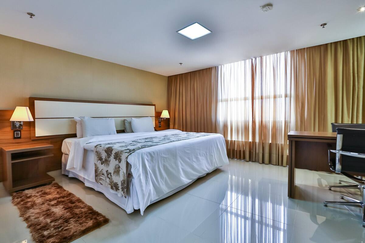 A hotel room with a bed, bedside lamps, a desk, and a chair.