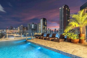 A rooftop pool with lounge chairs and potted plants, overlooking a cityscape at dusk. - SJ Premium By Atlantica (Goiania)