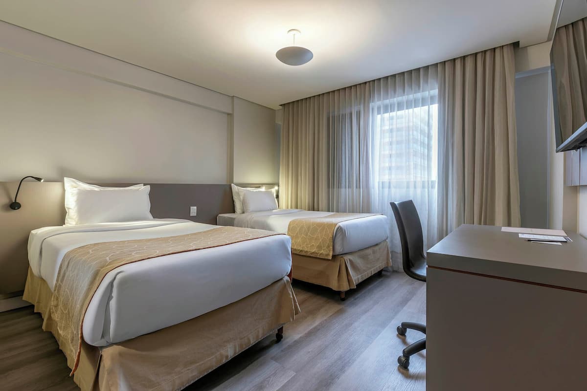 A hotel room with two beds, a desk, and a chair.