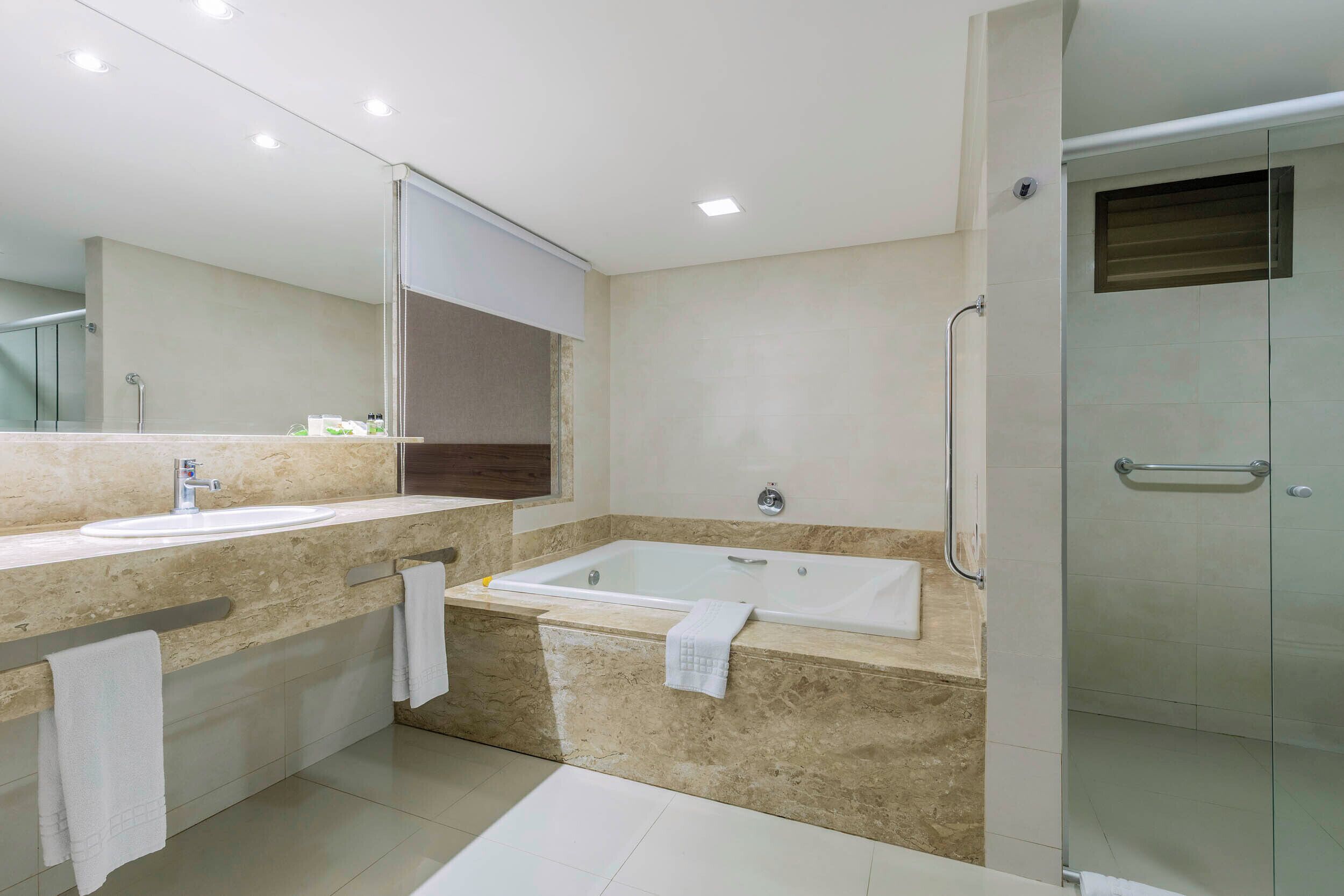 A modern bathroom with a large mirror, a bathtub, a shower, and a vanity with a sink.