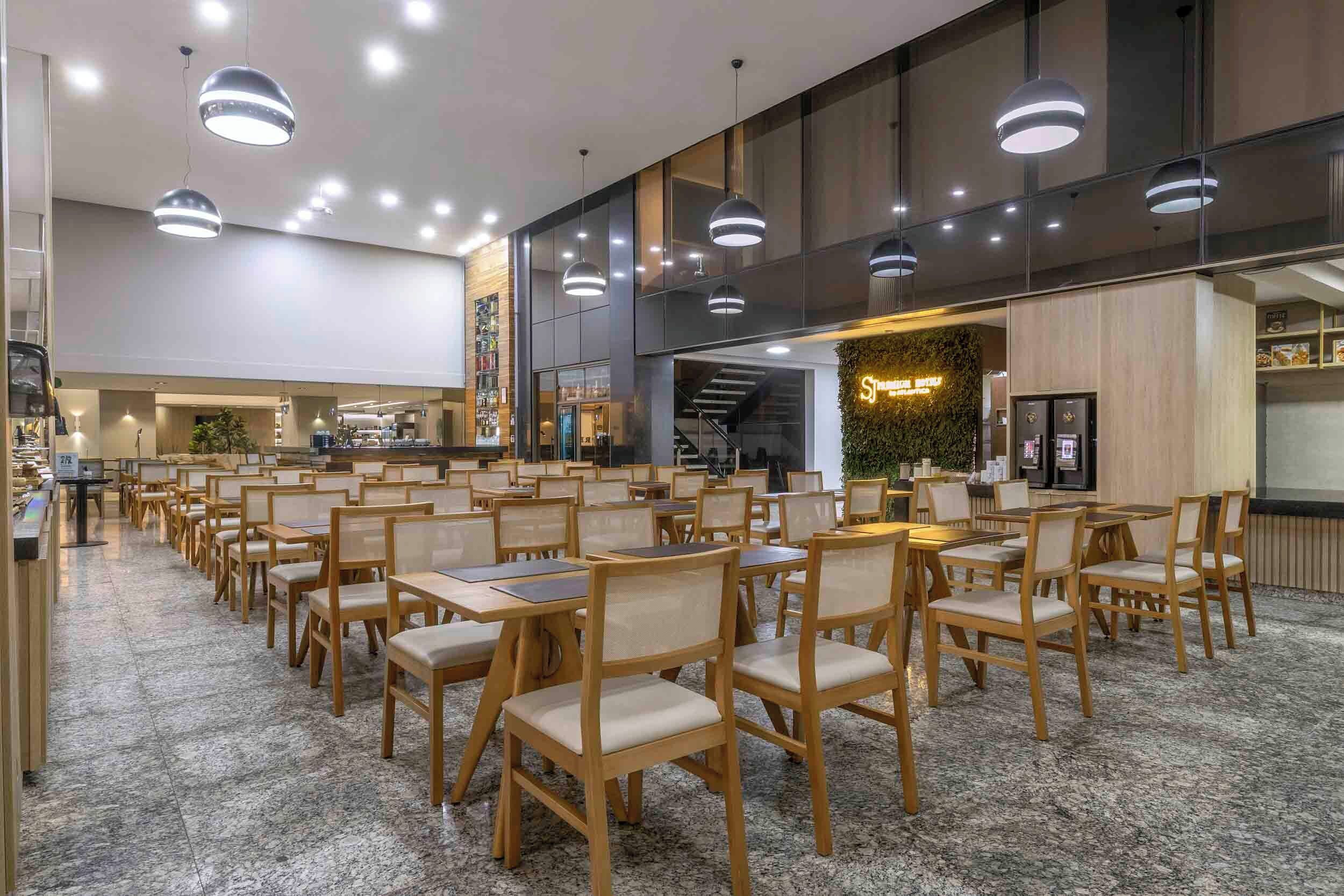 A spacious indoor area with multiple wooden tables and chairs, ceiling lights, and a staircase leading to an upper level.
