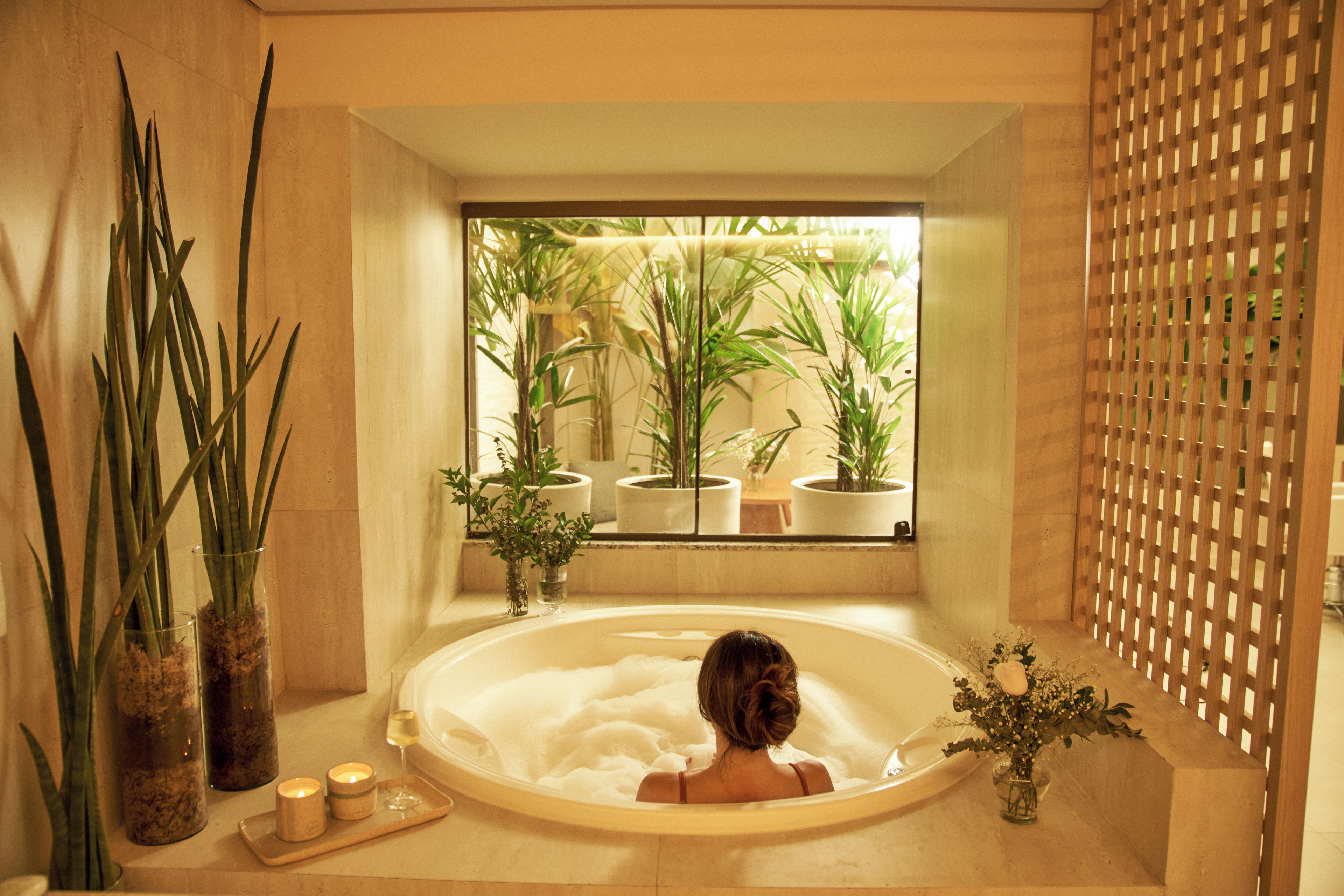 Un baño con bañera, plantas en macetas y una ventana.