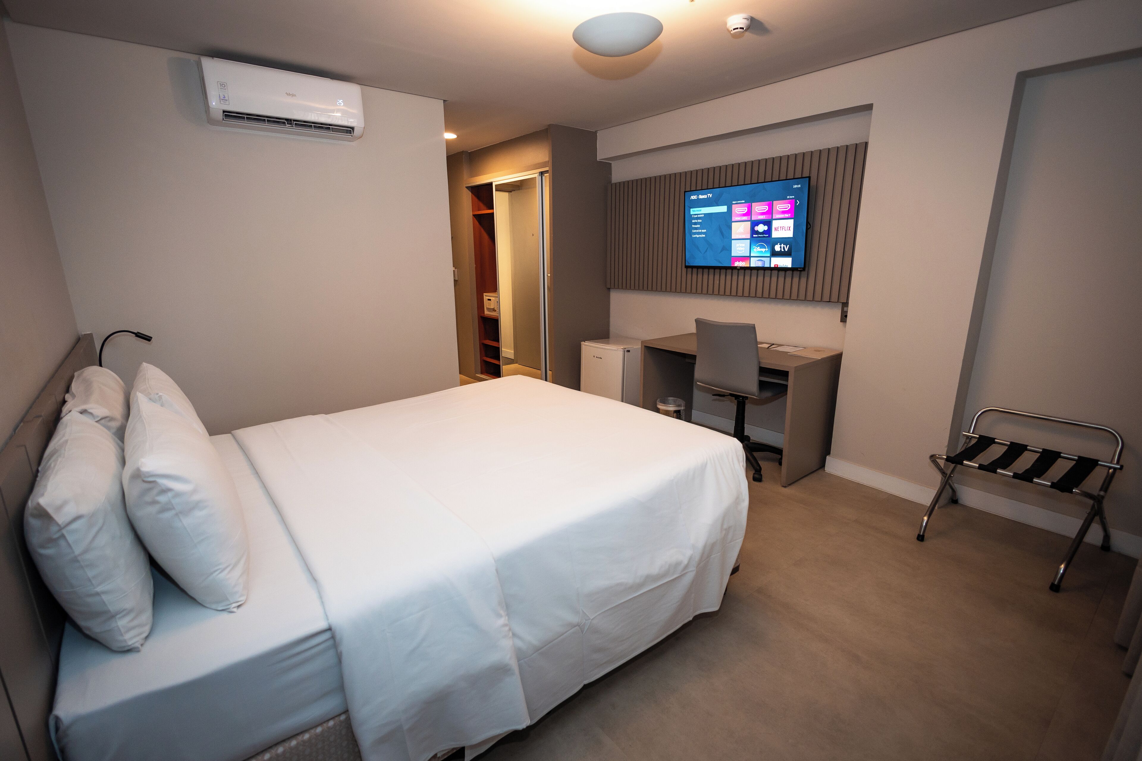 A hotel room with a bed, a desk, a chair, and a TV mounted on the wall.