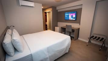 A hotel room with a bed, a desk, a chair, and a TV mounted on the wall.