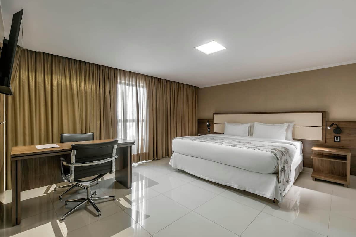 A hotel room with a bed, desk, chair, and nightstands.