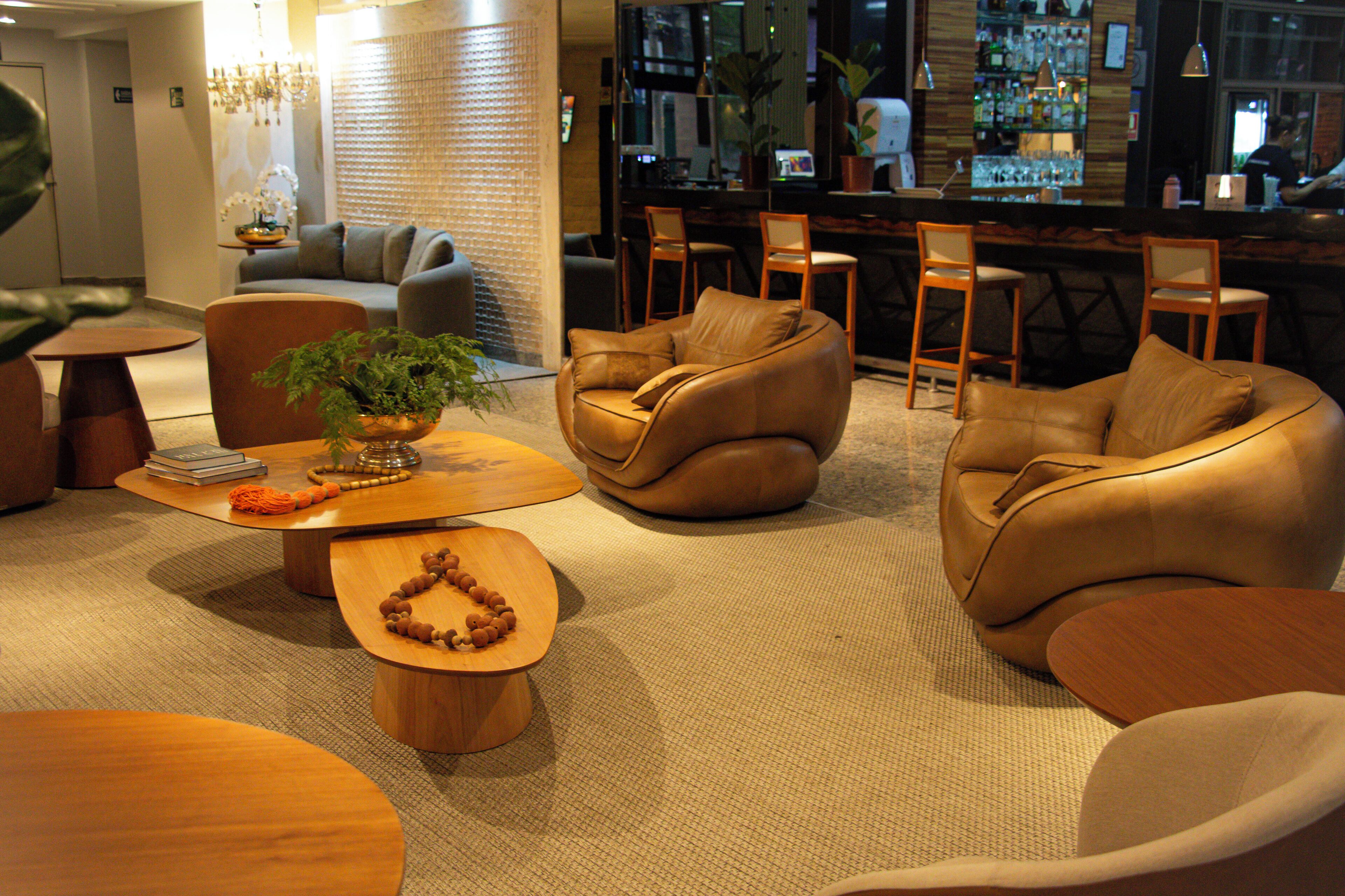 A modern hotel lobby with leather sofas, a wooden coffee table, and a bar area in the background.