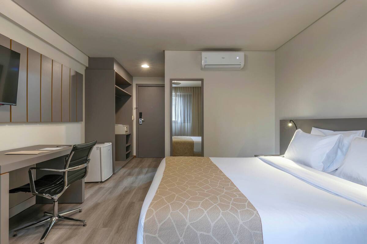 A hotel room with a bed, desk, chair, wardrobe, and a television.