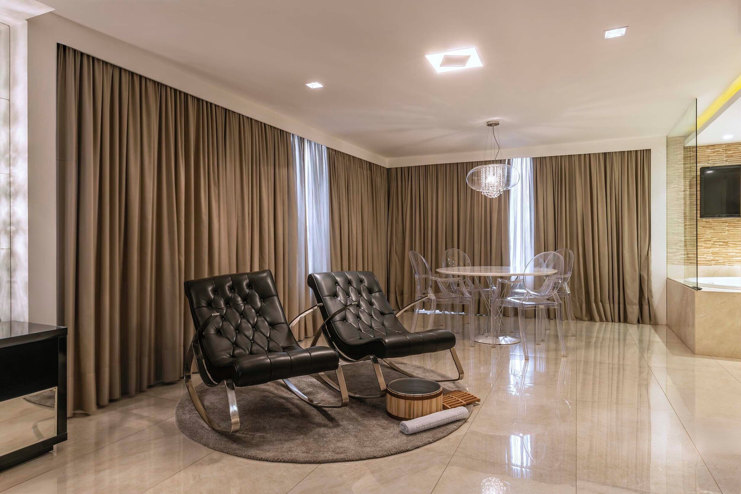 A modern living room with a sofa, a dining table with chairs, and a chandelier.