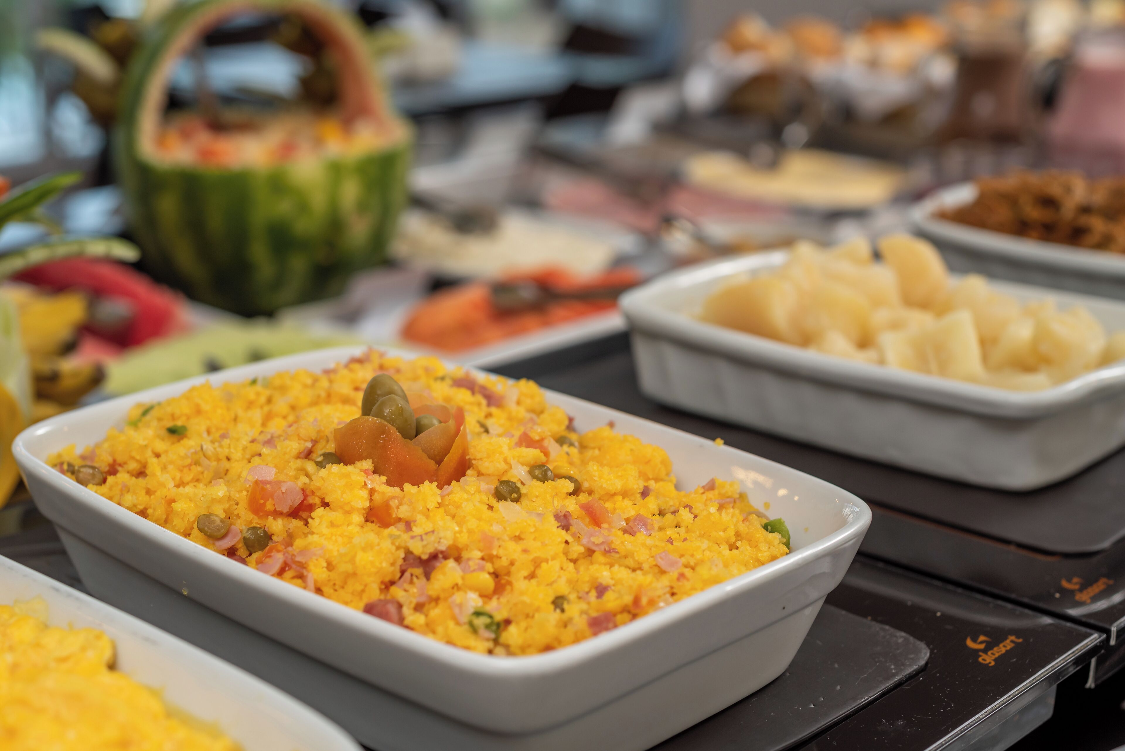 Buffet com diversos pratos, incluindo um prato de arroz amarelo com legumes e presunto.