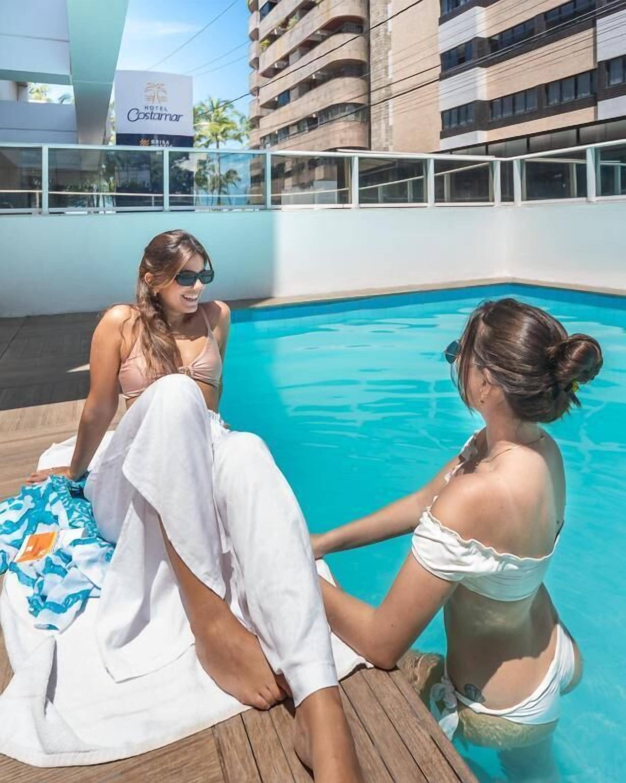 Zwei Personen an einem Pool, im Hintergrund ein Gebäude.