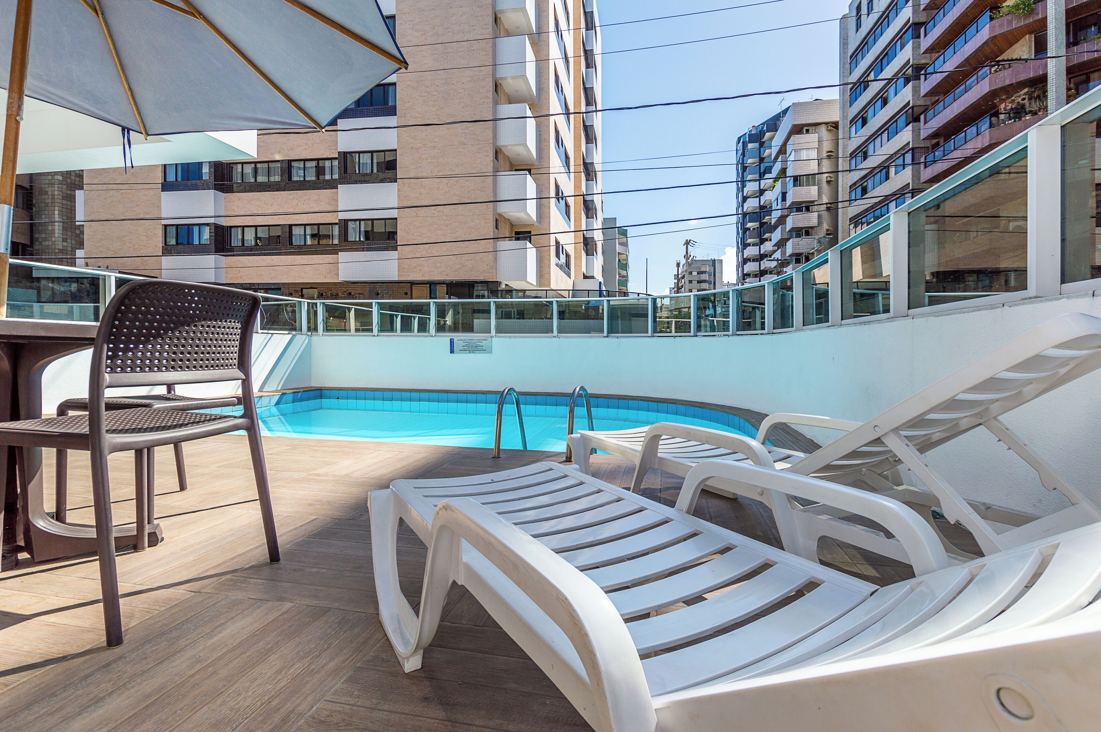 A rooftop pool area with lounge chairs and a table, surrounded by high-rise buildings.