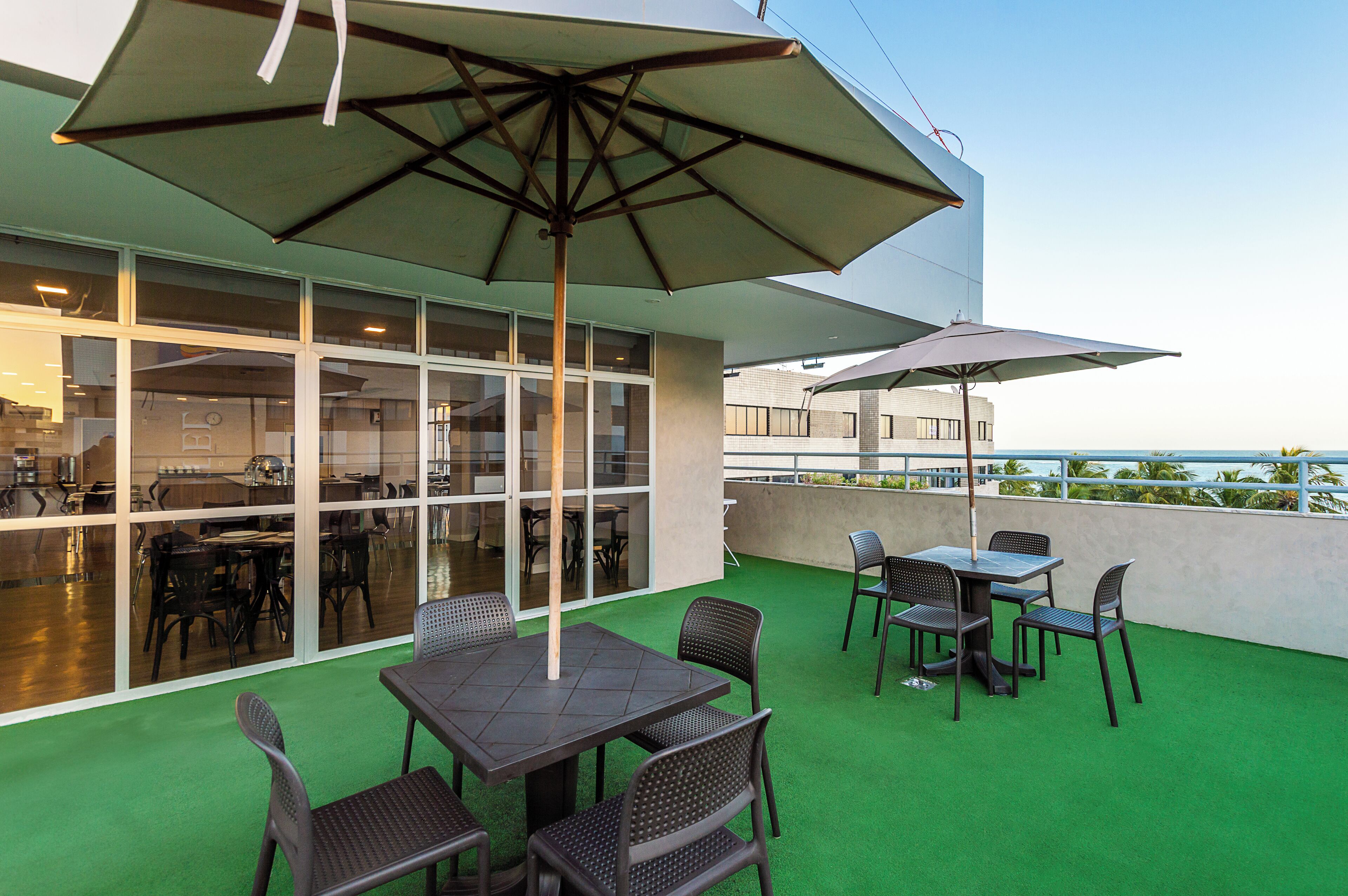 An outdoor patio area with tables and chairs, large umbrellas, and a view of the ocean.