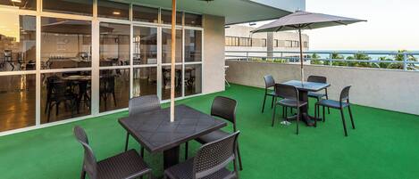 An outdoor patio area with tables and chairs, large umbrellas, and a view of the ocean.