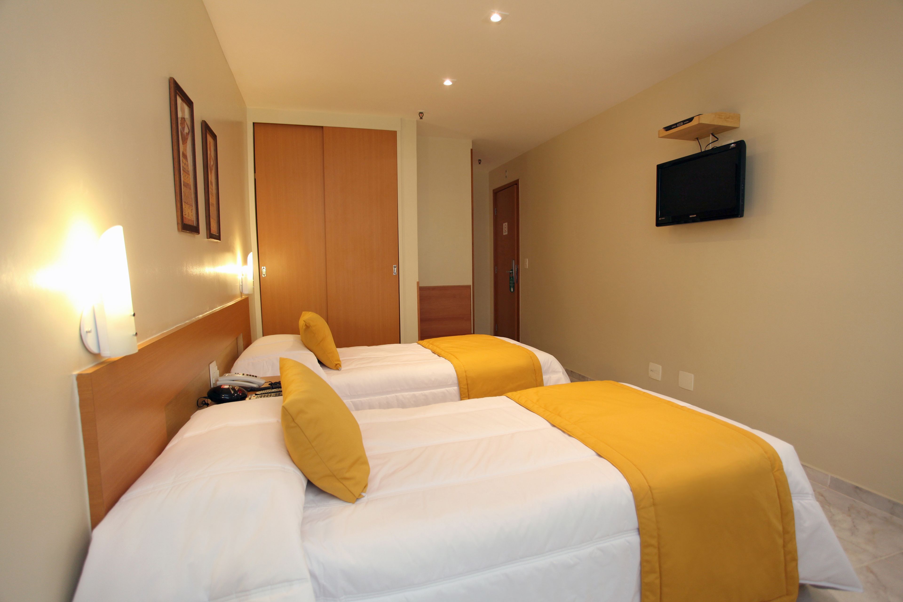 A hotel room with two beds, a TV mounted on the wall, and a wooden wardrobe.