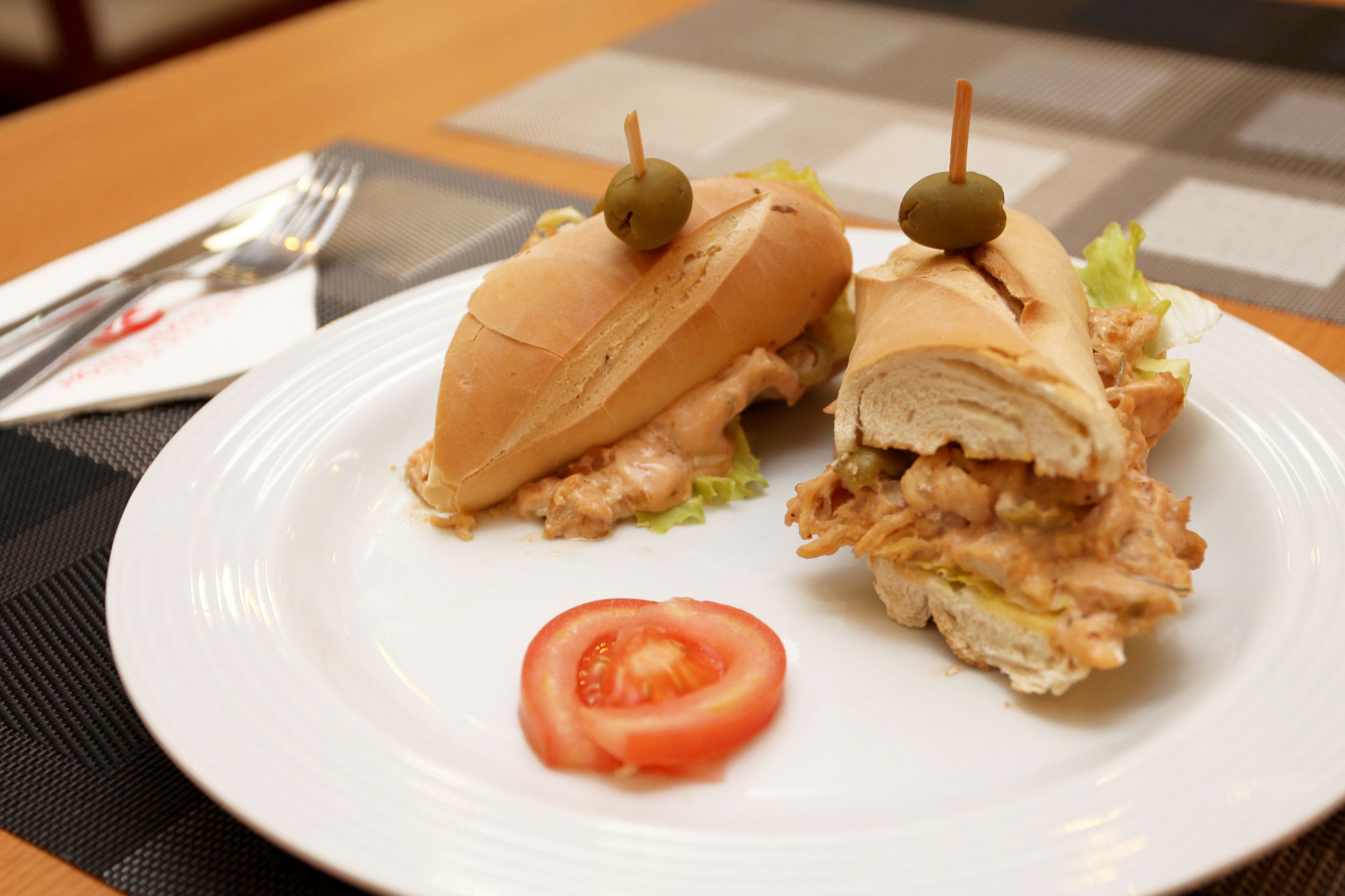 A sandwich on a white plate with a slice of tomato.