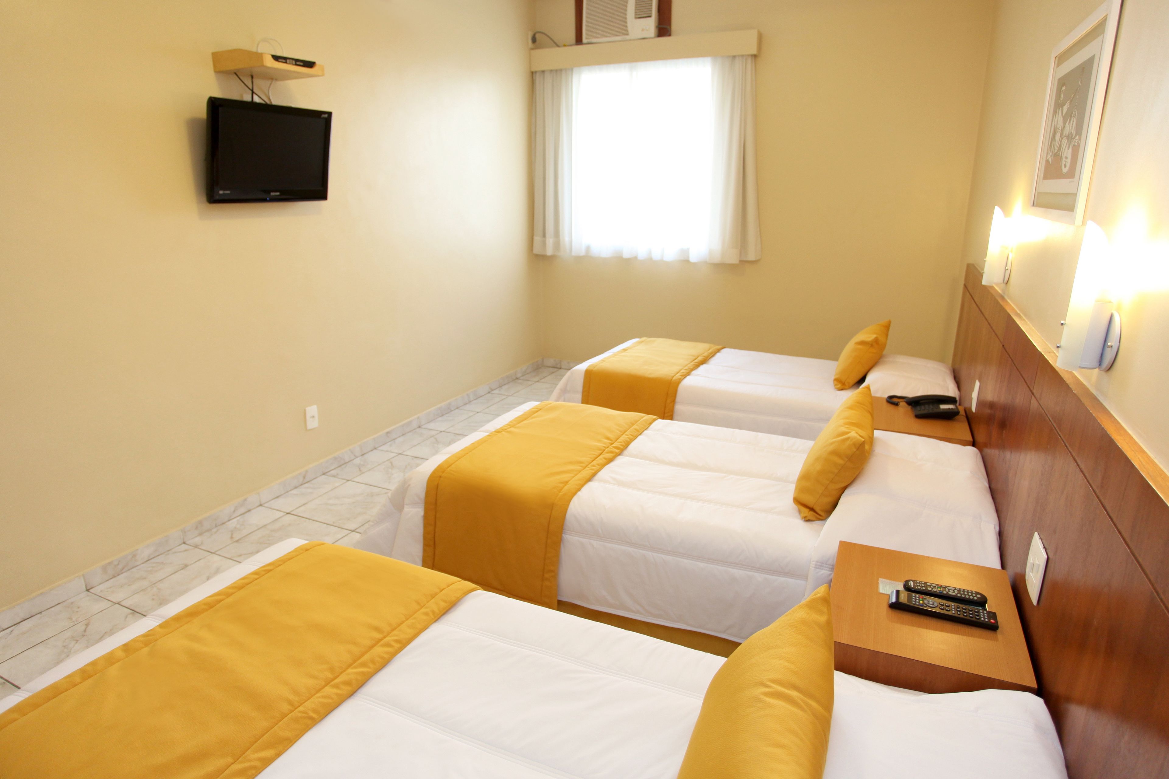 Habitación de hotel con dos camas, un televisor montado en la pared y una ventana con cortinas.