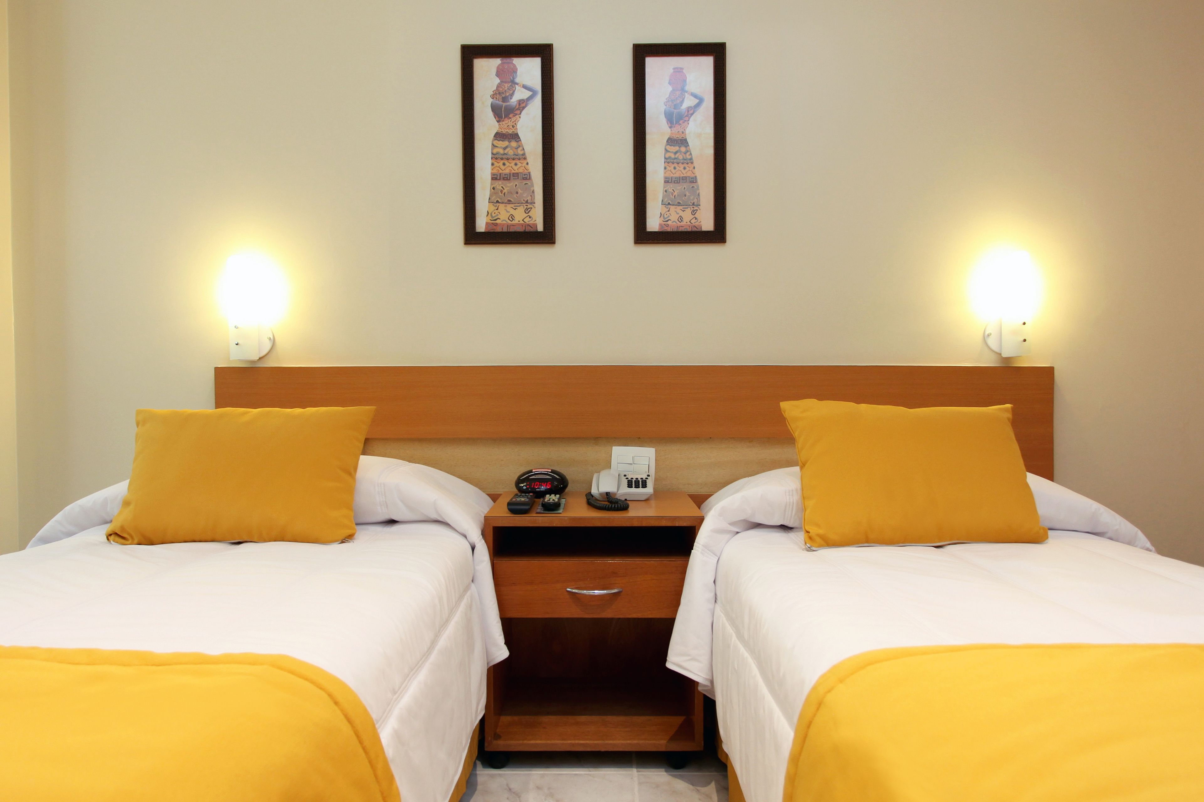 A hotel room with two beds, a wooden headboard, bedside tables with lamps, a telephone, and a drawer.