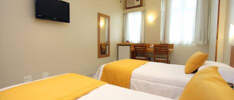A hotel room with two beds, a television mounted on the wall, a desk, and a window with curtains.