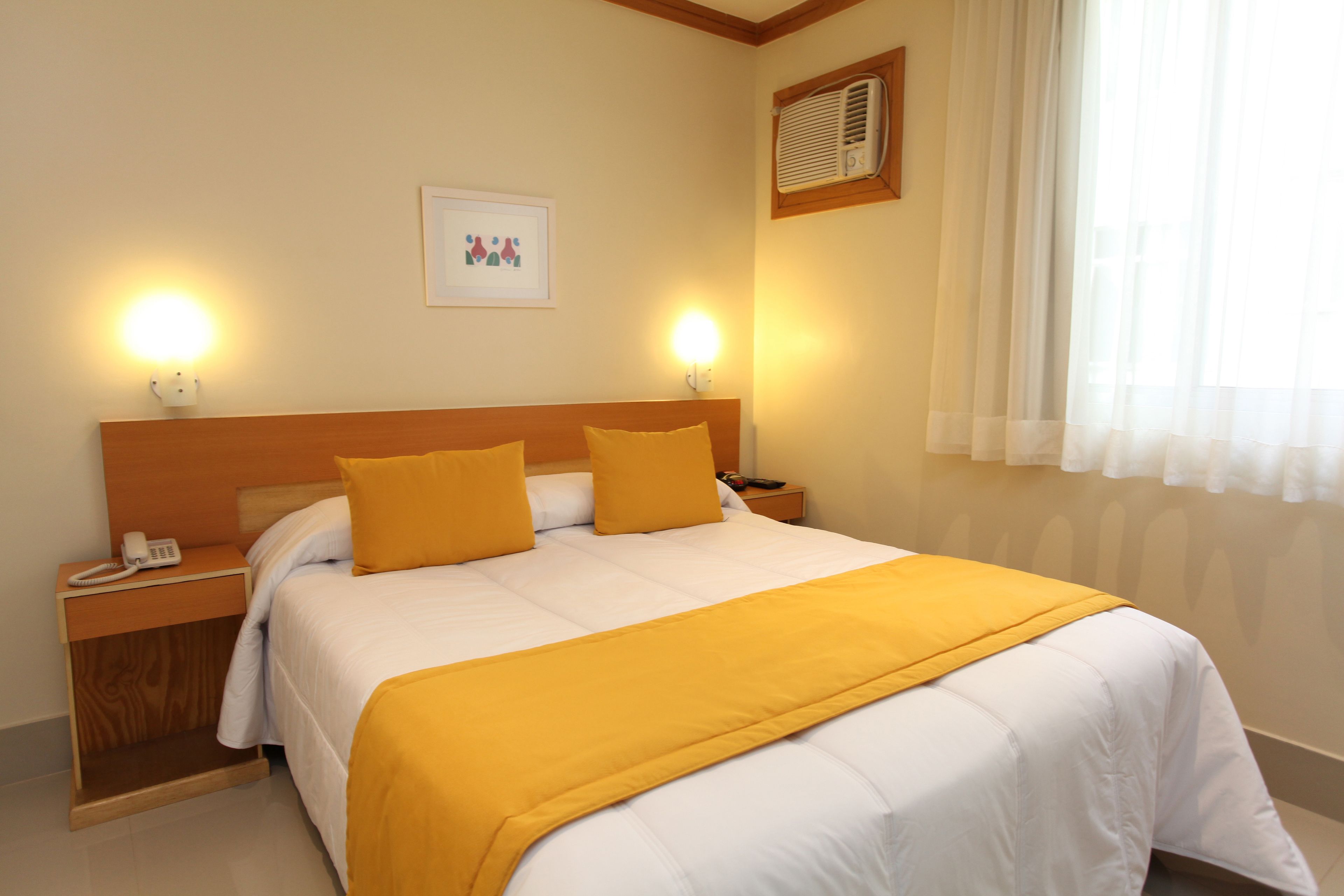 A hotel room with a bed, bedside lamps, a nightstand with a phone, and a window with curtains.